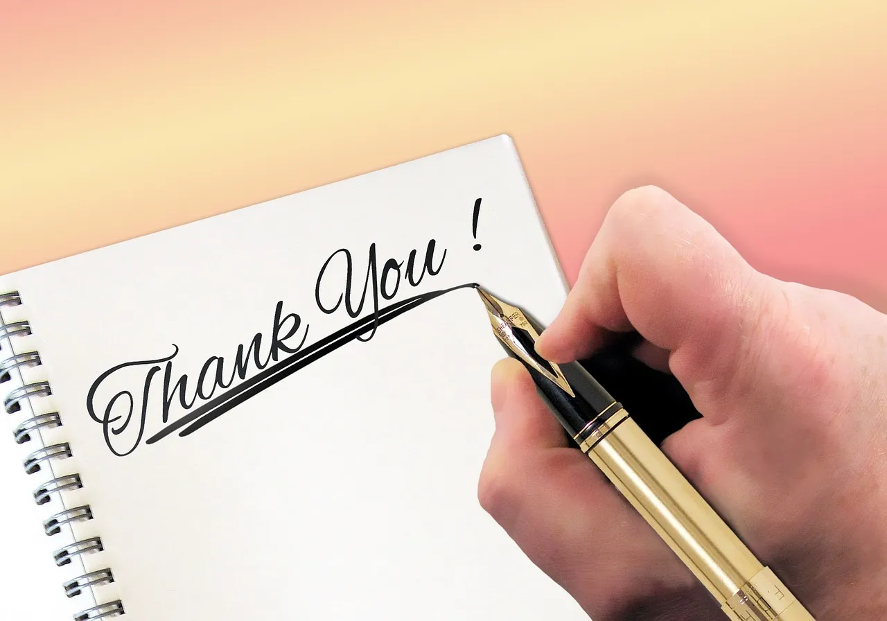Image of a hand just finishing writing thank you in a notebook